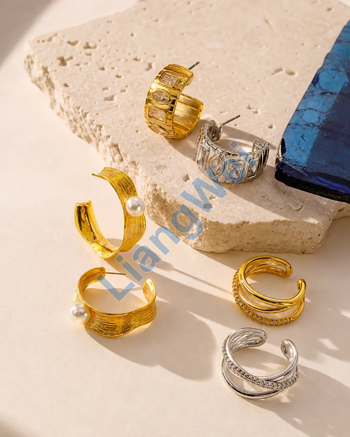 Fashion earrings and rings styled on warm ivory stone with cobalt glass